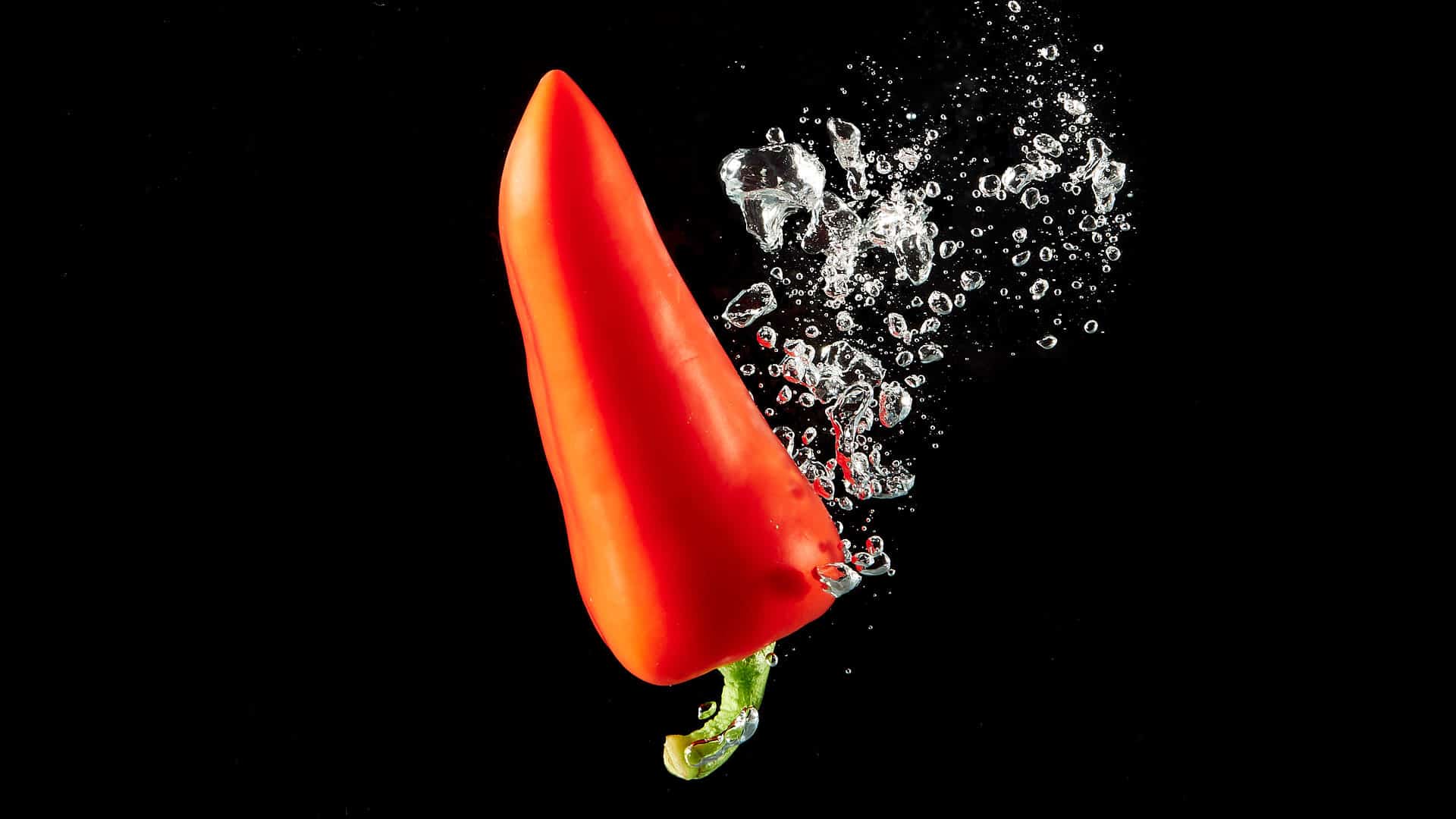 Sweet red pepper splashed in water on black background.