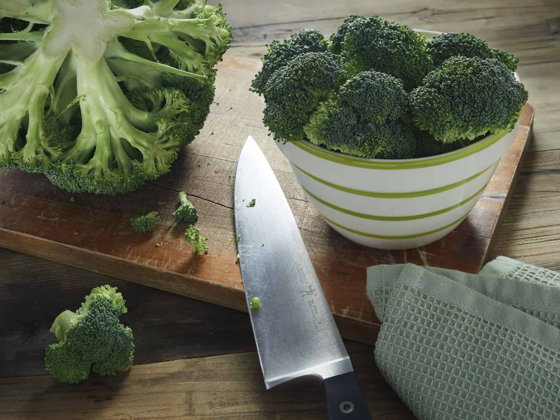 Broccoli head with florets on cutting board with knife